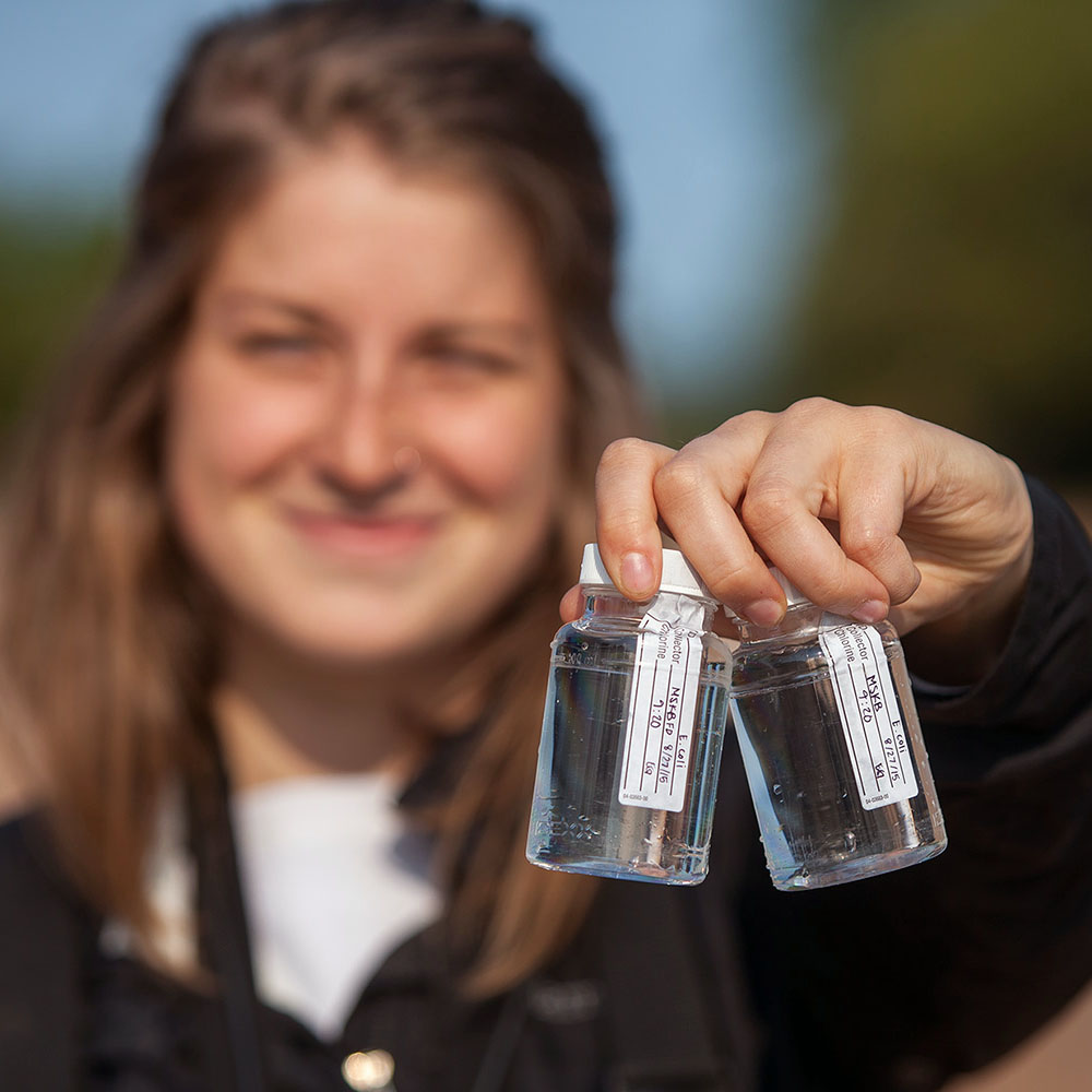 Student holding out water sample bottles toward the camera